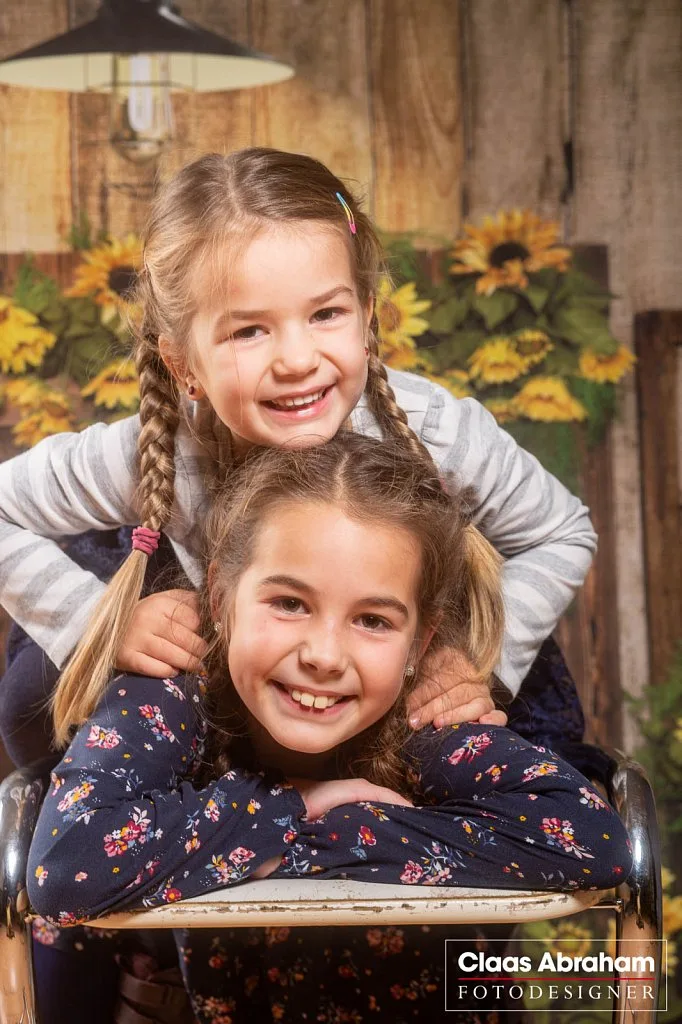 Zwei lachende Schwestern auf einem Stuhl im Fotostudio.
